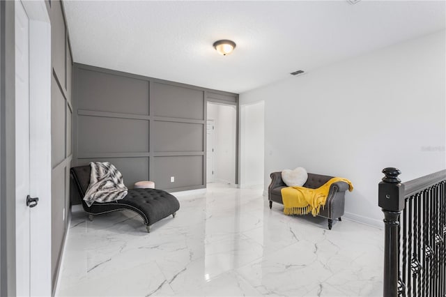 living area with visible vents, baseboards, a decorative wall, marble finish floor, and a textured ceiling