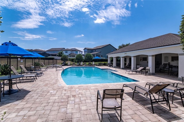 community pool featuring a patio area, fence, a residential view, and an outbuilding