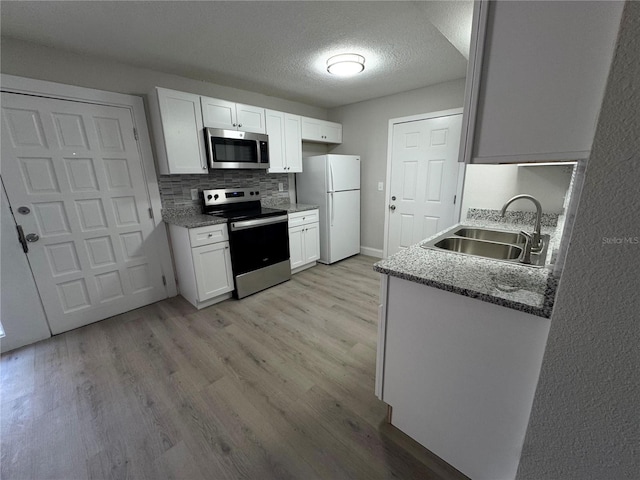 kitchen with light wood-style flooring, appliances with stainless steel finishes, white cabinetry, and a sink