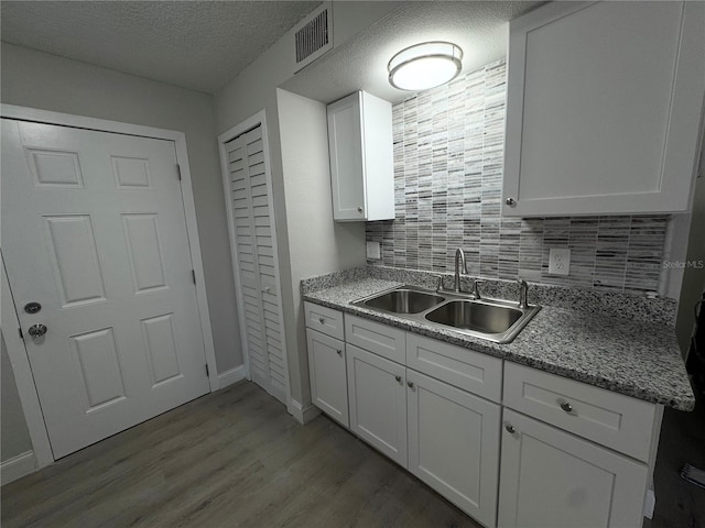 kitchen with visible vents, a sink, a textured ceiling, wood finished floors, and white cabinetry