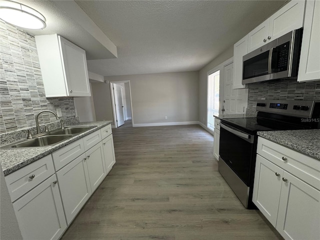 kitchen featuring a sink, tasteful backsplash, white cabinetry, stainless steel appliances, and light wood-style floors