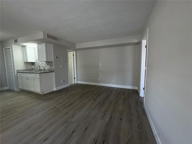 unfurnished living room with visible vents, baseboards, a textured ceiling, and dark wood-style floors