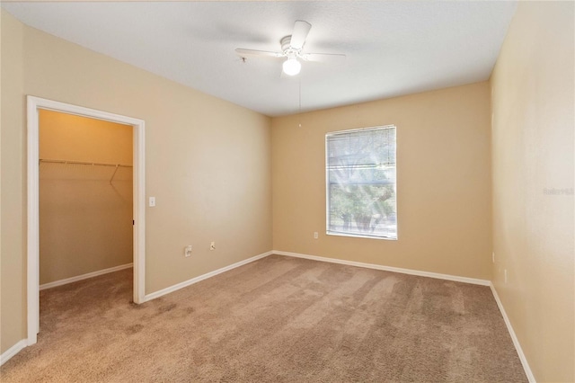 unfurnished bedroom featuring a walk in closet, baseboards, carpet, a closet, and a ceiling fan