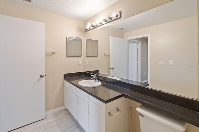 bathroom featuring vanity, baseboards, visible vents, a textured ceiling, and toilet