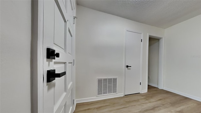 empty room with baseboards, visible vents, a textured ceiling, and light wood-style floors