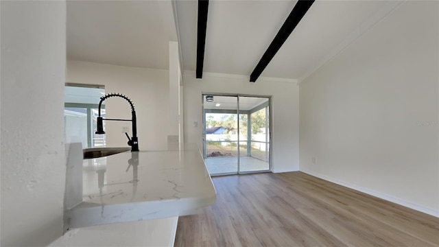 unfurnished living room with a sink, baseboards, beam ceiling, and wood finished floors