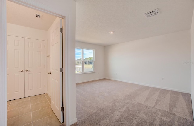 spare room with light tile patterned floors, light colored carpet, visible vents, and baseboards
