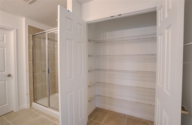 bathroom with tile patterned floors, a shower stall, a textured ceiling, and a walk in closet