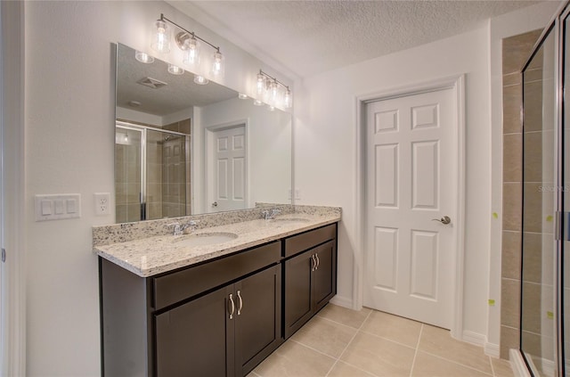 bathroom with double vanity, a stall shower, tile patterned floors, a textured ceiling, and a sink