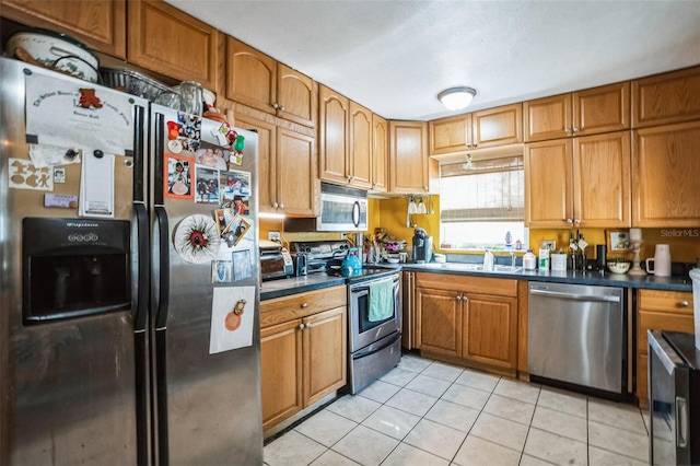 5224 29th Ave S, Gulfport, FL 33707 - kitchen featuring light tile patterned floors, brown cabinetry, a sink, stainless steel appliances, and dark countertops
