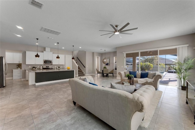 living room with stairs, light tile patterned floors, a ceiling fan, and visible vents