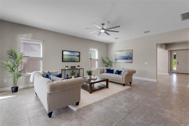 living room featuring light tile patterned floors, a ceiling fan, visible vents, and a textured ceiling