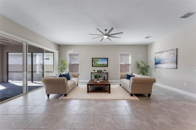 tiled living room featuring baseboards, a ceiling fan, visible vents, and a textured ceiling
