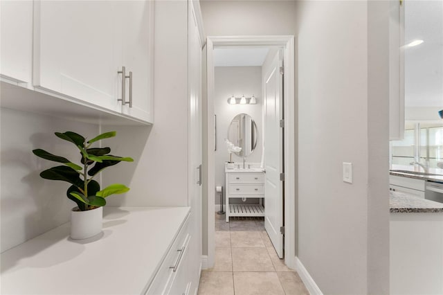 corridor featuring light tile patterned floors, baseboards, and a sink