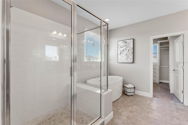 bathroom featuring tile patterned floors, a freestanding tub, a walk in closet, a stall shower, and baseboards