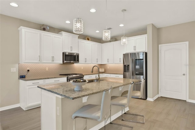 kitchen with a breakfast bar area, light stone counters, stainless steel appliances, white cabinetry, and backsplash