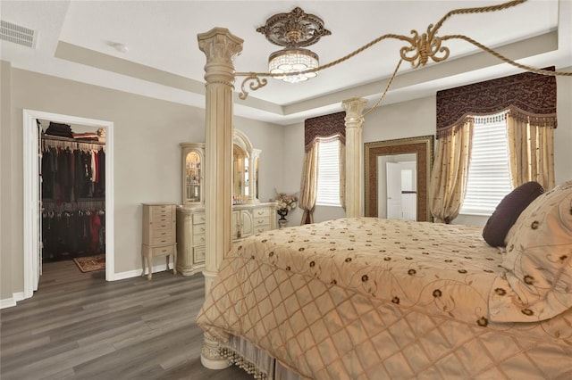 bedroom featuring wood finished floors, visible vents, baseboards, a tray ceiling, and a spacious closet