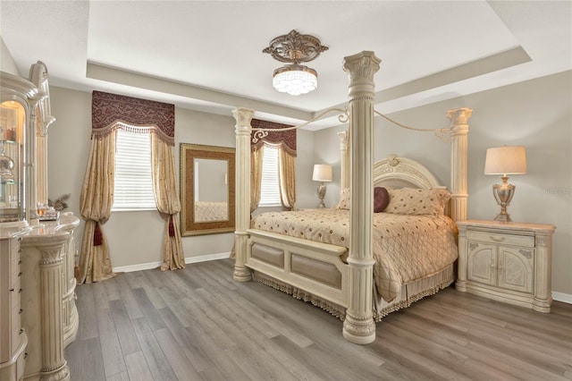 bedroom with a raised ceiling, wood finished floors, and baseboards