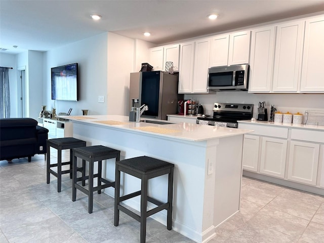 kitchen featuring a center island with sink, appliances with stainless steel finishes, a breakfast bar area, and white cabinets