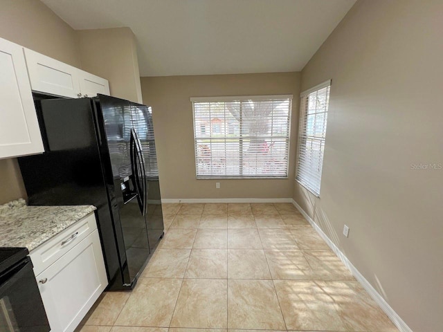 kitchen featuring baseboards, light stone countertops, vaulted ceiling, light tile patterned floors, and white cabinetry