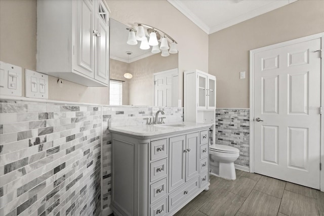 bathroom with ornamental molding, toilet, tile walls, vanity, and wainscoting