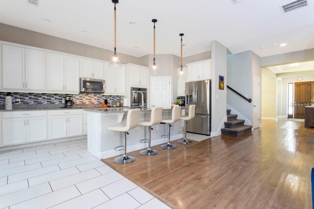 14645 Scott Key Dr, Winter Garden, FL 34787 - kitchen with visible vents, stainless steel appliances, white cabinets, a kitchen bar, and tasteful backsplash