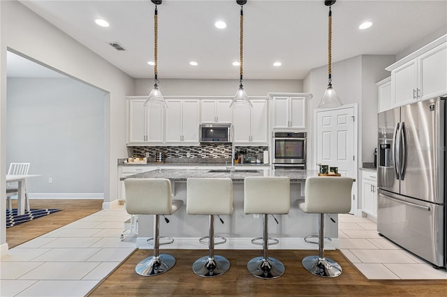14645 Scott Key Dr, Winter Garden, FL 34787 - kitchen featuring a kitchen island with sink, decorative backsplash, appliances with stainless steel finishes, and white cabinets