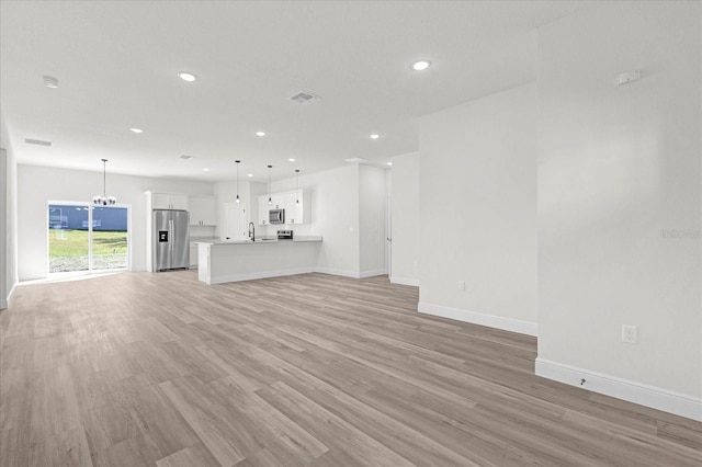unfurnished living room featuring light wood-style flooring, a notable chandelier, recessed lighting, and baseboards