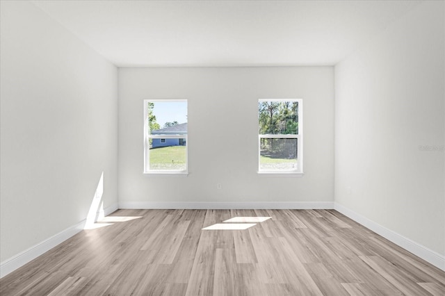 spare room with light wood finished floors, a healthy amount of sunlight, and baseboards