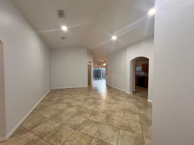 unfurnished room featuring light tile patterned floors, visible vents, baseboards, lofted ceiling, and arched walkways