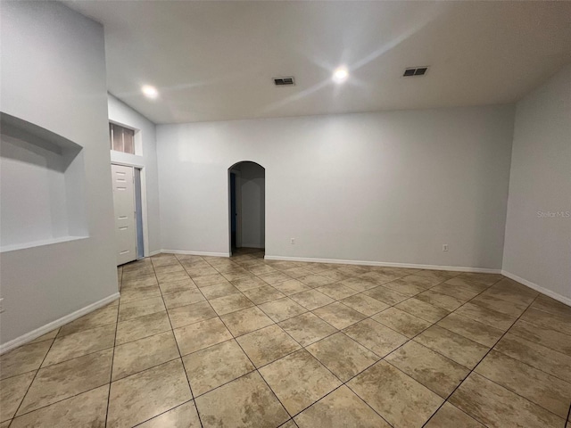 empty room with light tile patterned floors, arched walkways, visible vents, and baseboards