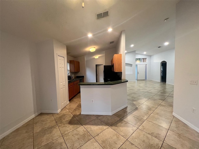 kitchen featuring visible vents, black refrigerator, dark countertops, arched walkways, and vaulted ceiling