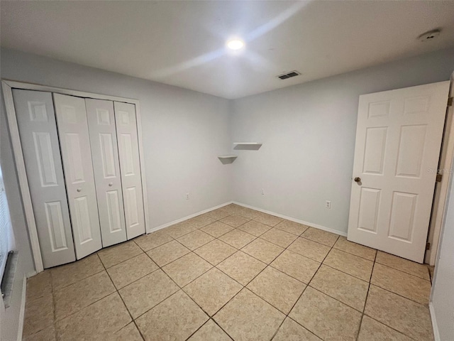 unfurnished bedroom with light tile patterned floors, visible vents, a closet, and baseboards