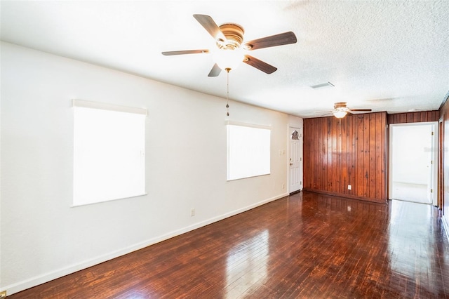 empty room with baseboards, ceiling fan, wood walls, a textured ceiling, and wood-type flooring