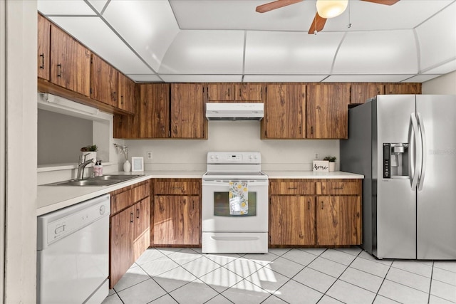 kitchen featuring under cabinet range hood, a sink, white appliances, light tile patterned flooring, and light countertops