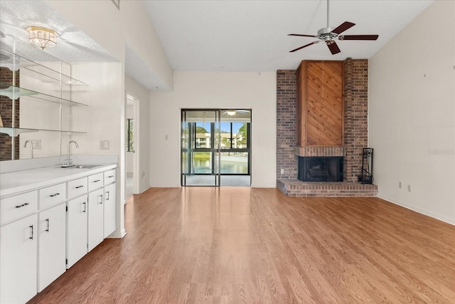 unfurnished living room with a ceiling fan, lofted ceiling, a sink, a brick fireplace, and light wood-type flooring