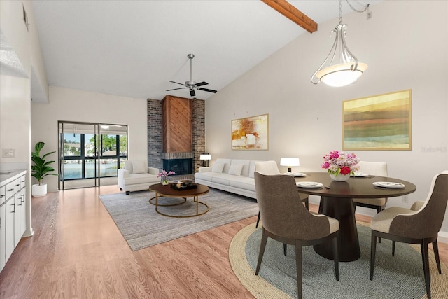 dining area with beamed ceiling, a fireplace, light wood-style floors, high vaulted ceiling, and a ceiling fan