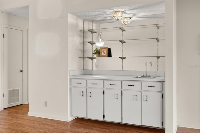 bar with wood finished floors, visible vents, wet bar, a sink, and a textured ceiling