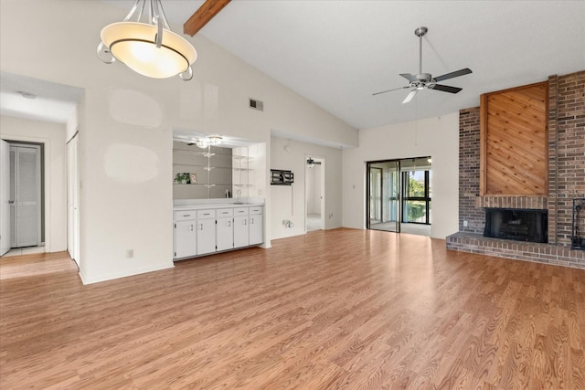 unfurnished living room with visible vents, a brick fireplace, ceiling fan, light wood-style floors, and high vaulted ceiling