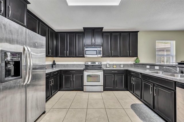 5910 Windsong Oak Dr, Leesburg, FL 34748 - kitchen with stainless steel appliances, dark cabinetry, light tile patterned flooring, a textured ceiling, and a sink