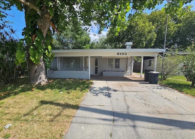 view of front facade featuring a front lawn, covered porch, concrete block siding, a carport, and driveway
