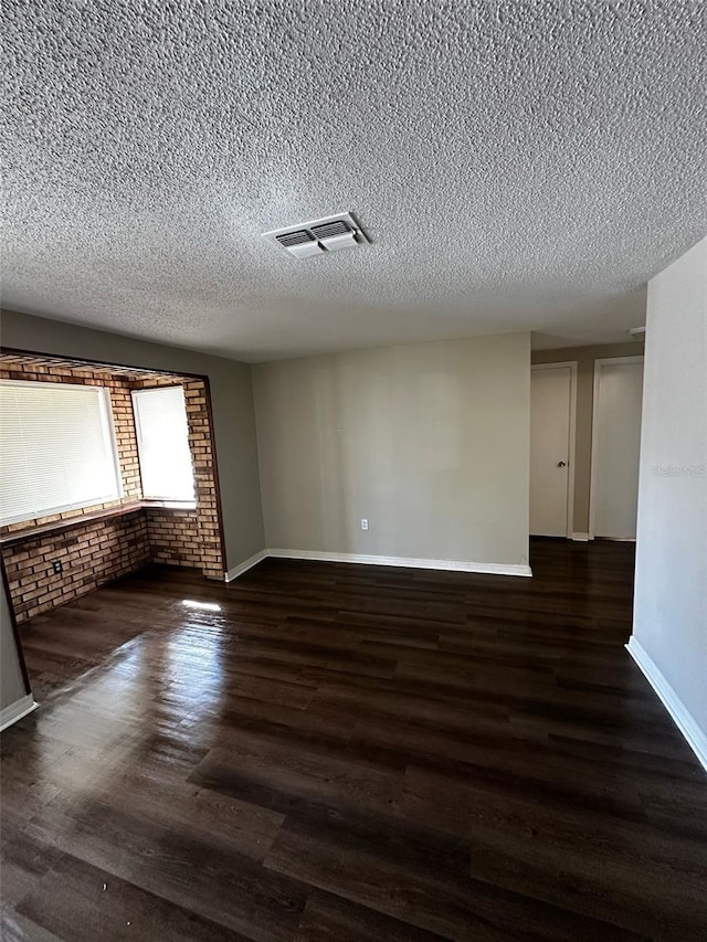 spare room featuring wood finished floors, baseboards, visible vents, brick wall, and a textured ceiling