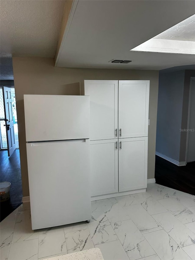 interior space with baseboards, freestanding refrigerator, white cabinets, a textured ceiling, and marble finish floor