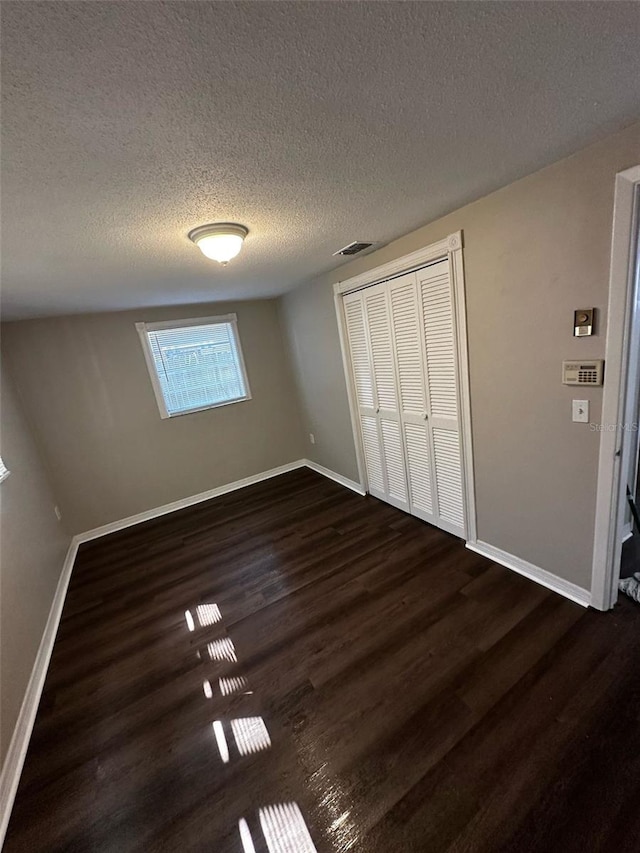 unfurnished bedroom featuring visible vents, baseboards, dark wood-type flooring, a closet, and a textured ceiling