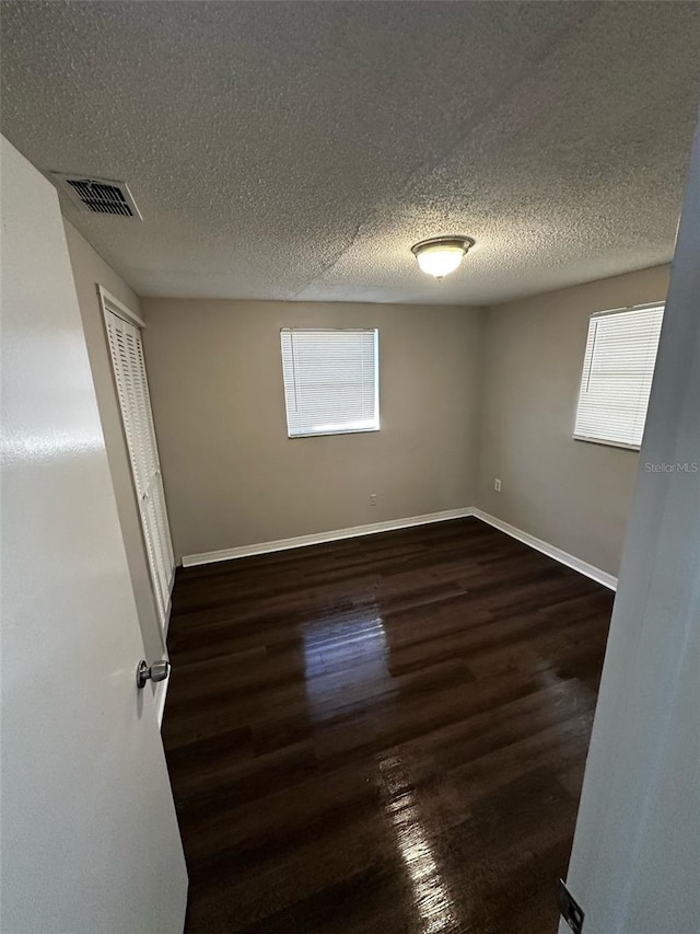 spare room with dark wood-style floors, visible vents, a textured ceiling, and baseboards