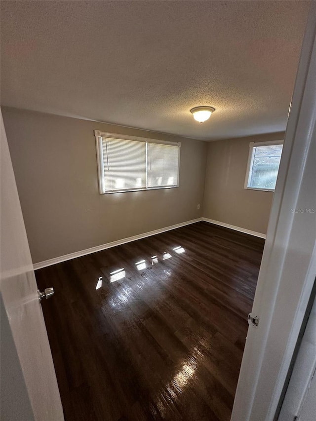 unfurnished room featuring dark wood-style floors, baseboards, and a textured ceiling