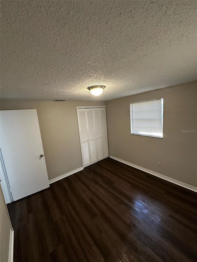 unfurnished bedroom featuring a closet, a textured ceiling, dark wood-type flooring, and baseboards