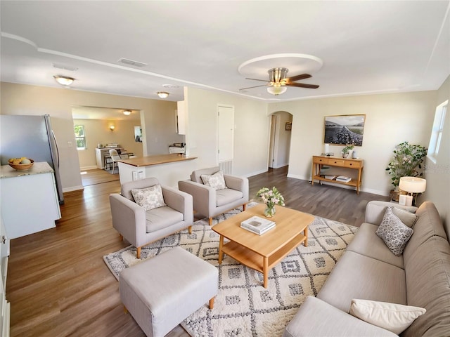 living room featuring baseboards, arched walkways, visible vents, ceiling fan, and wood finished floors
