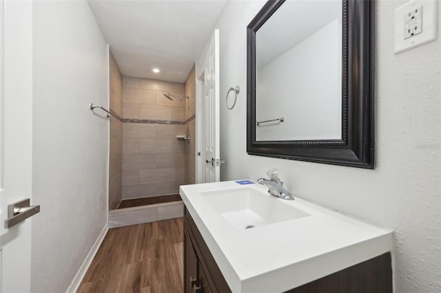bathroom featuring vanity, baseboards, wood finished floors, and tiled shower