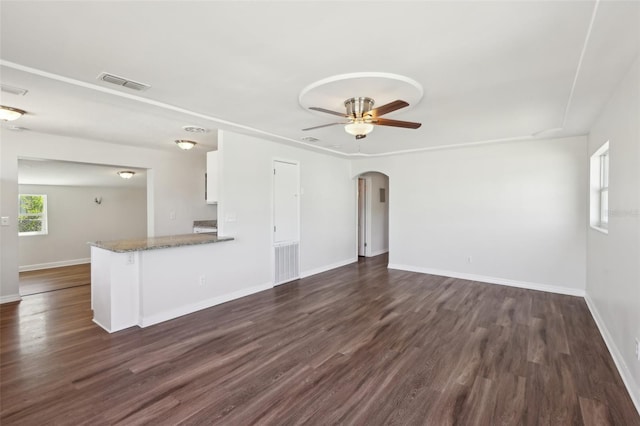 unfurnished living room featuring dark wood finished floors, arched walkways, ceiling fan, and visible vents